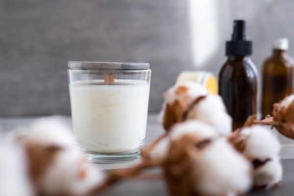 A photo of a soy candle with a flower and essential oils next to it