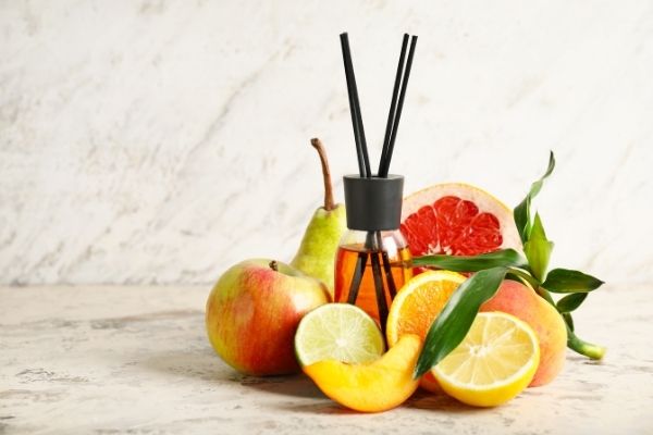 A photo of a reed diffuser surrounded by fruits